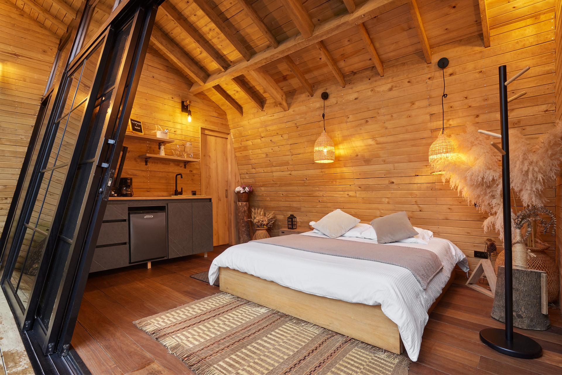Interior en madera de la cabaña Ceiba con cama y luces cálidas