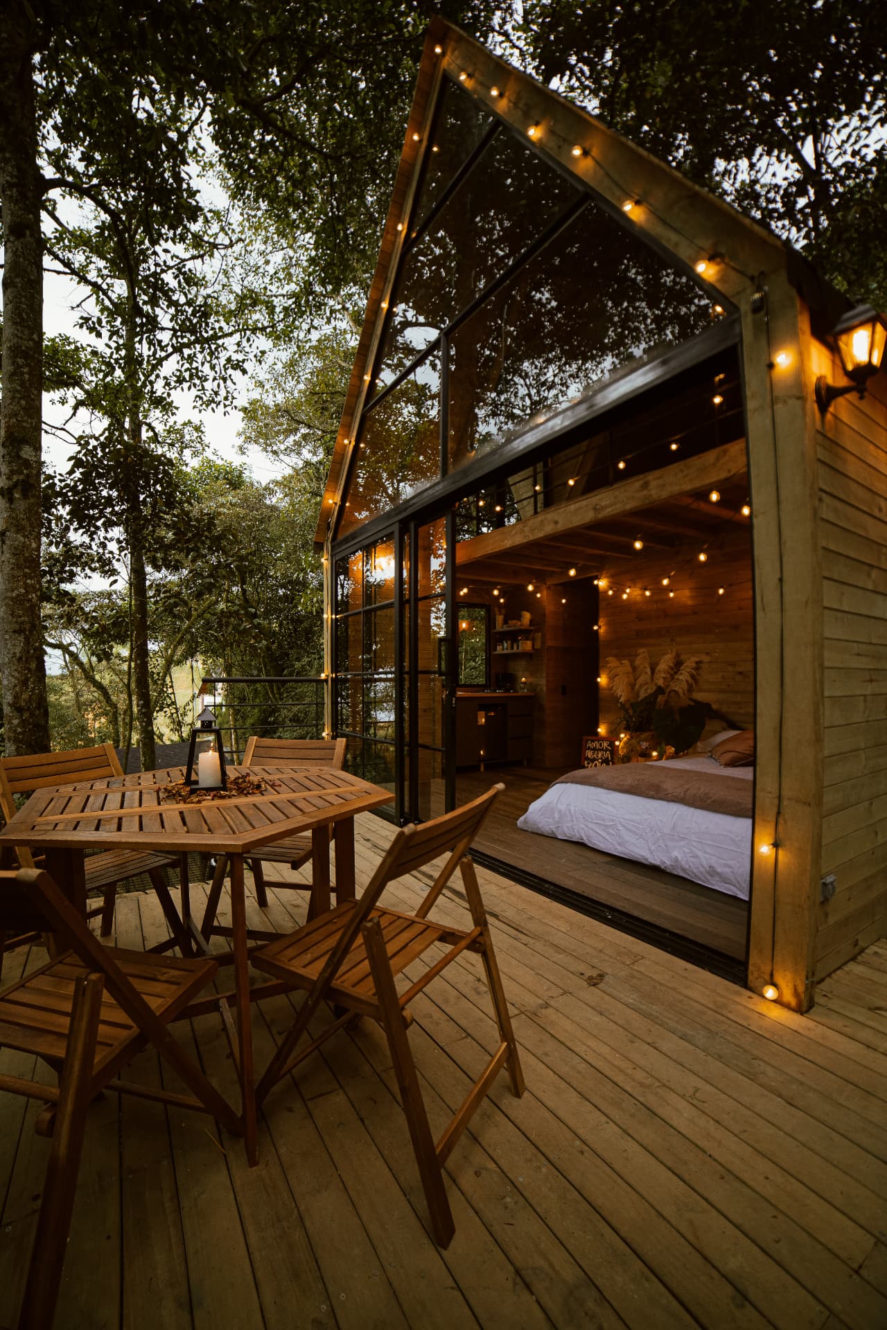 Interior de la cabaña Cedro visto desde la terraza, con cama, cocina y ventanales abiertos al bosque