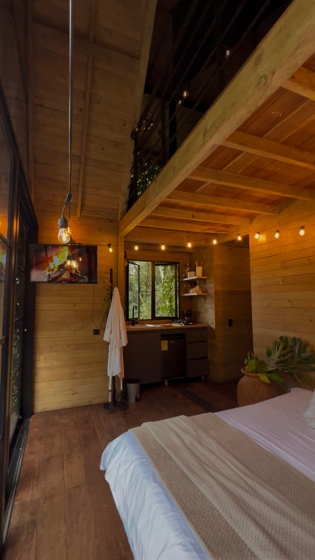 Interior de la cabaña Cedro con cama, cocina dotada, televisor y altillo de madera