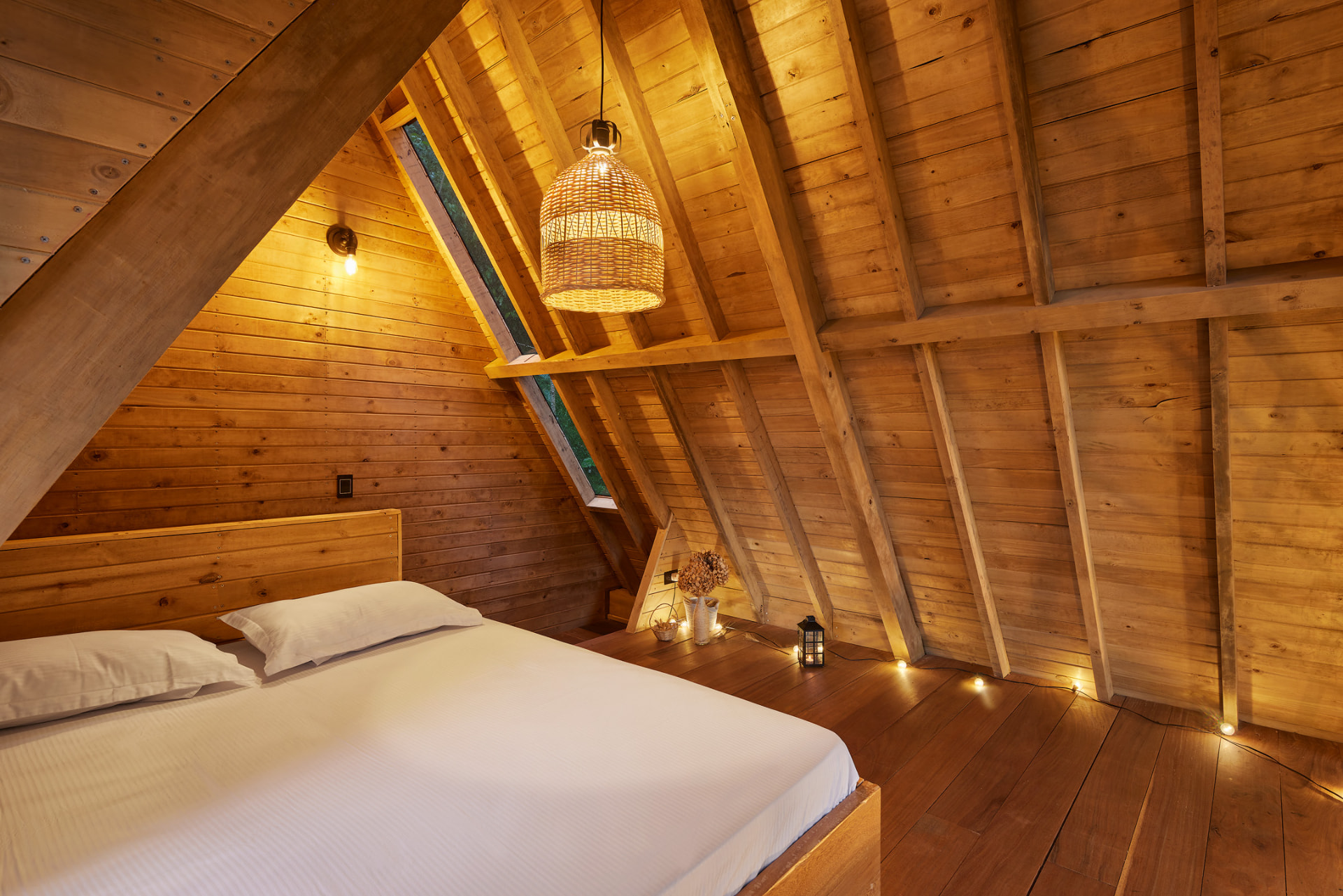 Altillo de la cabaña Cedro con cama de ropaje blanco bajo techo de madera inclinado