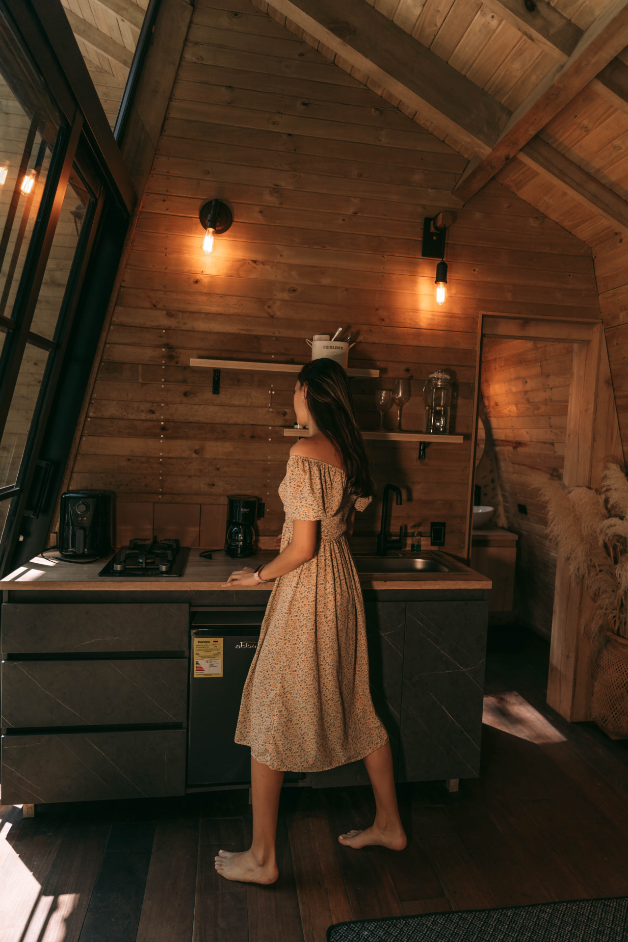 Cocina dotada en madera de la cabaña Gardenia con luz cálida y ventanal al bosque